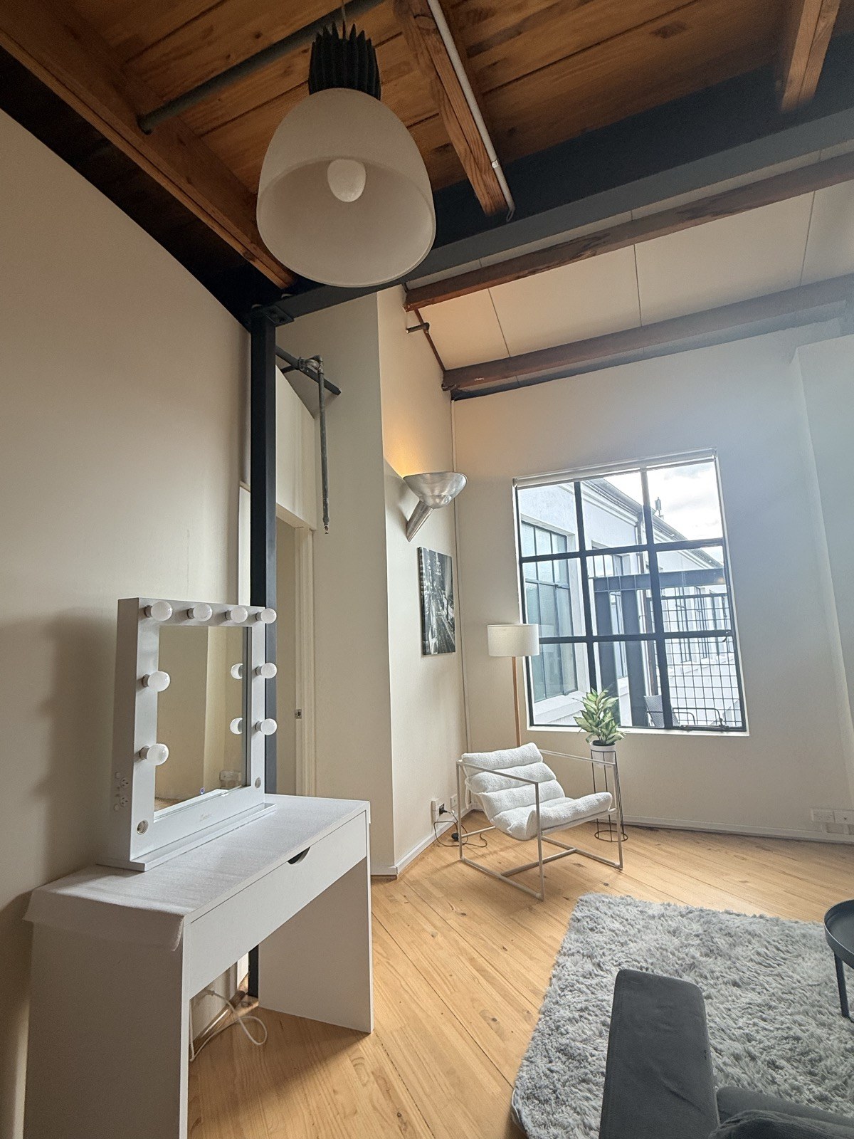 A getting-ready vanity with mirror lights beside the tall loft windows